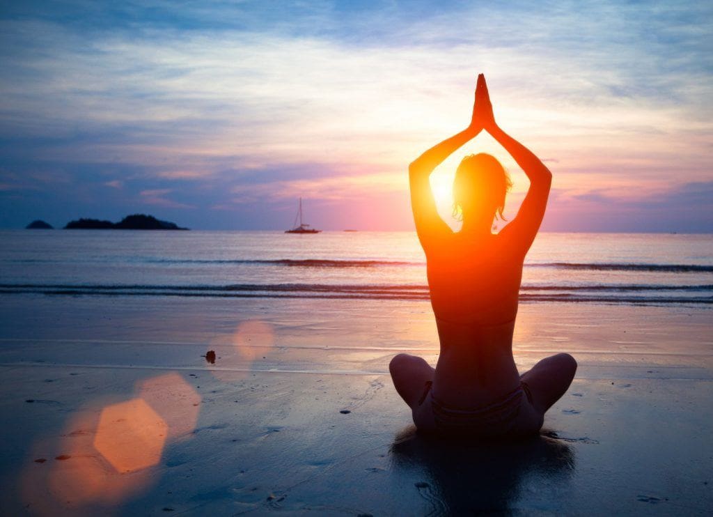 woman doing yoga on beach at sunset