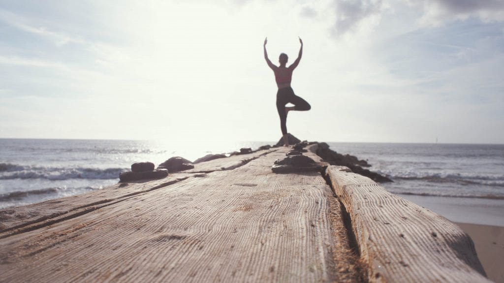 woman doing yogo on wood at beach at sunrise