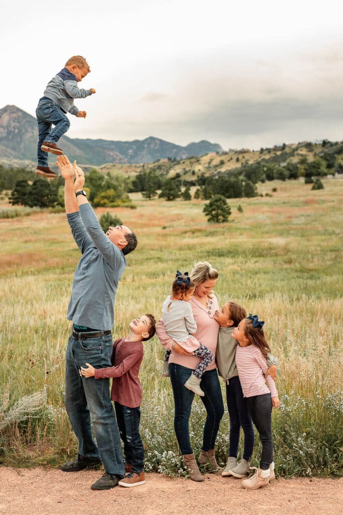 A family smiling and looking at each other for a portrait. Green grass and mountains in the background. 