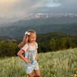 A little girl running through a green grass oasis. Surrounded by mountains and blue skies. A client of Dr. Ryan at Radix Chirorpactic.