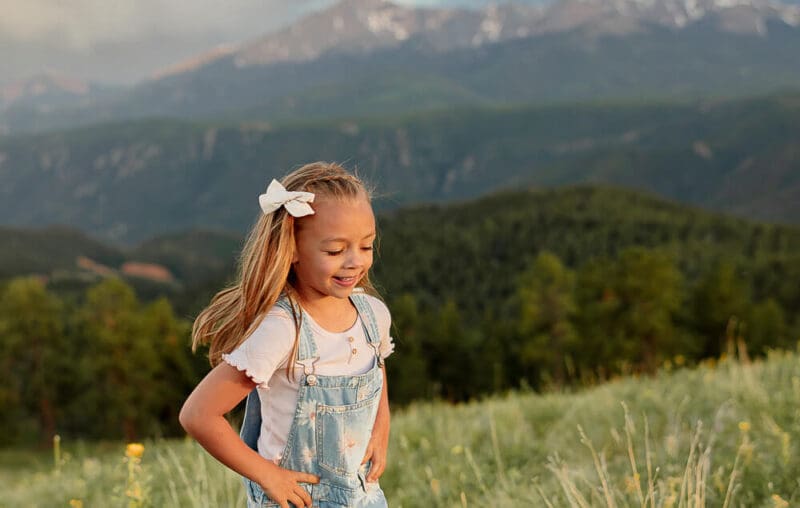 A little girl running through a green grass oasis. Surrounded by mountains and blue skies. A client of Dr. Ryan at Radix Chirorpactic.