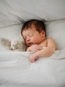 A little baby snuggled in a bed, with a stuffy. Captured by Michelle Betz Photography