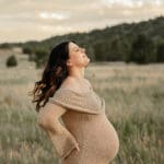 A pregnant women, holding her back and shaking out her hair. Surrounded by Colorado Springs mountains.