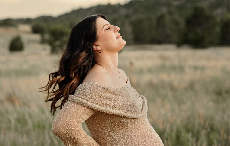 A pregnant women, holding her back and shaking out her hair. Surrounded by Colorado Springs mountains.