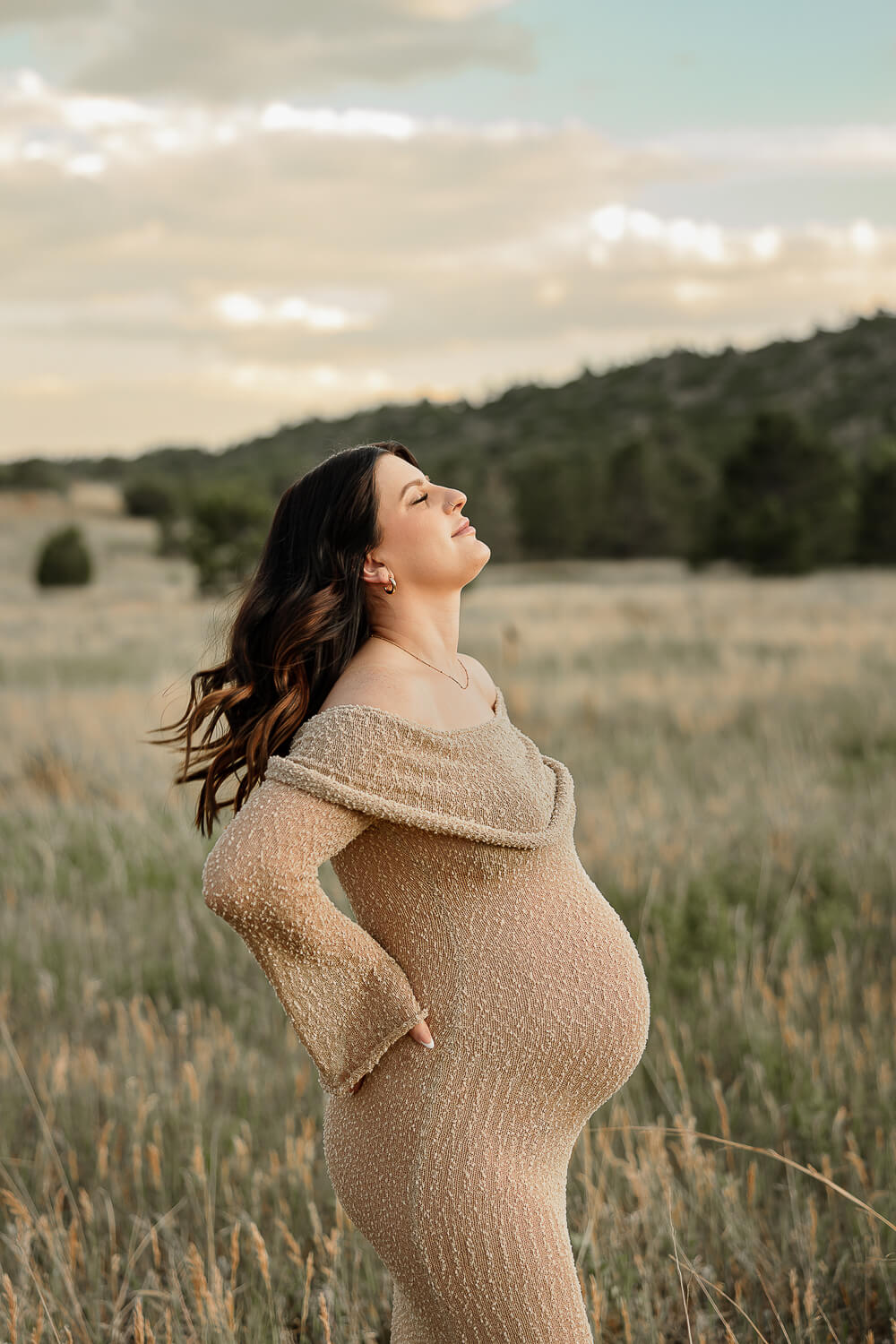 A pregnant women, holding her back and shaking out her hair. Surrounded by Colorado Springs mountains.